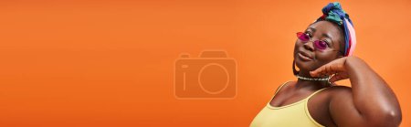 Fashionable plus size african american woman in headscarf and trendy sunglasses on orange, banner