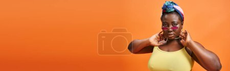 stylische plus size afrikanisch-amerikanische Frau mit Kopftuch und trendiger Sonnenbrille auf orangefarbenem Banner