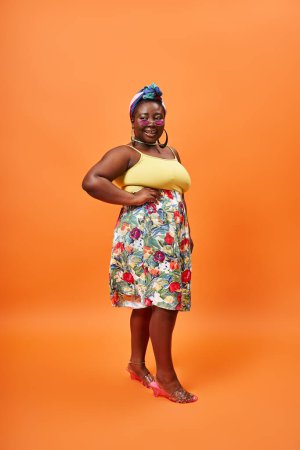 plus size african american model in floral outfit and sunglasses posing with hand on hip on orange