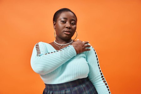 Photo for Confident plus size african american woman in plaid skirt and blue long sleeve on orange background - Royalty Free Image