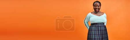 Téléchargez les photos : Corps positif femme afro-américaine en jupe à carreaux et bleu manches longues souriant sur orange, bannière - en image libre de droit