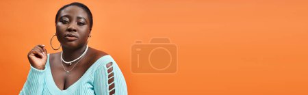 Photo for Body positive african american woman in plaid skirt and blue long sleeve looking at camera, banner - Royalty Free Image