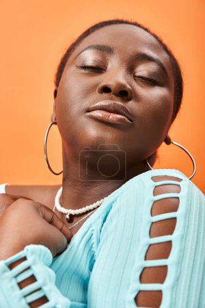 retrato de bonita mujer afroamericana de talla grande en manga larga azul posando sobre fondo naranja