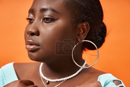 portrait de femme afro-américaine taille plus en bleu manches longues posant sur fond orange, dramatique
