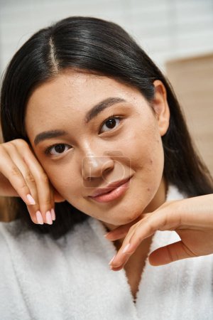 close up of happy young asian woman with acne touching face and looking at camera, skin care