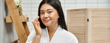 happy asian woman with acne applying cream on face and smiling while looking at camera, banner