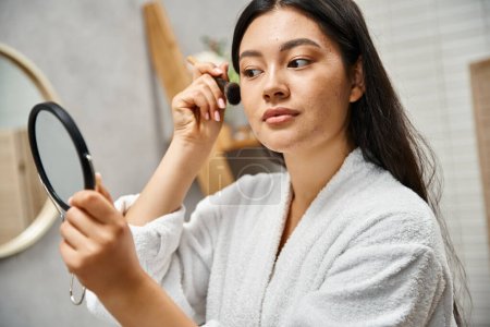 pretty asian woman with brunette hair applying makeup over acne-prone skin with cosmetic brush