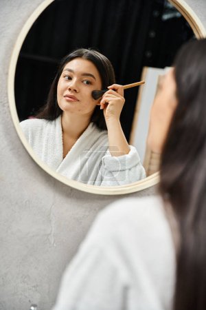 junge asiatische Frau, die Gesichtspuder mit Pinsel auf die zu Akne neigende Haut aufträgt, um Spiegel, Make-up anzusehen