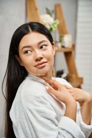 Porträt einer jungen Asiatin mit Akne-anfälliger Haut, die im modernen Badezimmer steht und wegschaut