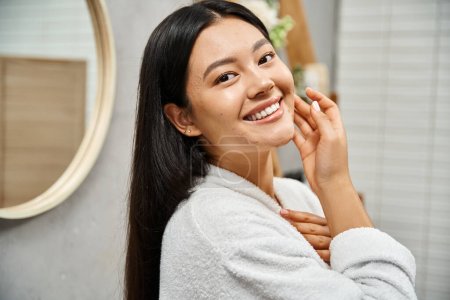 Foto de Retrato de feliz joven asiático con acné propenso piel de pie en moderno cuarto de baño y mirando a la cámara - Imagen libre de derechos