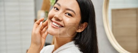 bannière de heureux jeune asiatique avec la peau sujette à l'acné debout dans la salle de bain moderne et en regardant la caméra
