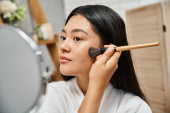 young asian woman with brunette hair and acne applying face powder and looking at mirror, skin issue puzzle #692759736