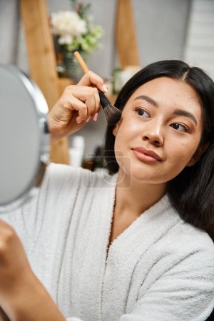 bonita y joven mujer asiática con manchas aplicando polvo facial y mirando al espejo, acné