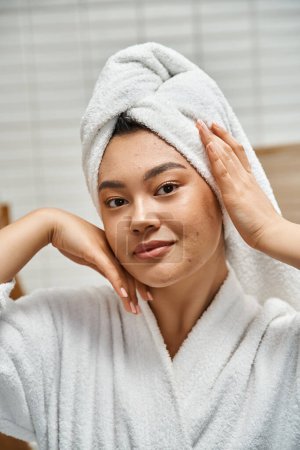 vertical shot of young asian woman with acne prone skin with white towel on head in bathroom