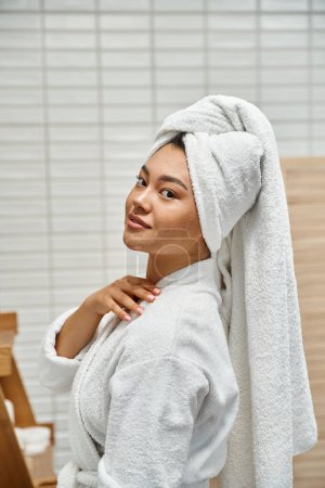 young asian woman with acne prone skin with white towel on head posing in bathroom at home