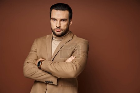 handsome man in turtleneck and blazer giving confident look while standing with folded arms on beige