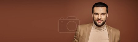 cheerful and handsome man with bristle posing in stylish beige blazer on beige backdrop, banner