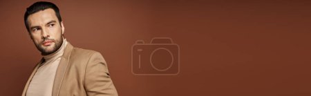 handsome man in elegant attire looking away while posing in blazer on beige background, banner mug #692773470