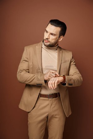 handsome man in elegant attire checking his wristwatch on beige background, time management
