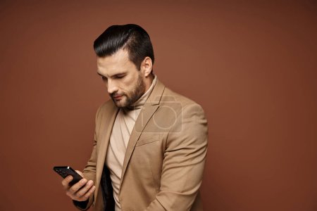 Téléchargez les photos : Bel homme d'affaires en tenue élégante vérifiant son smartphone sur fond beige, réseautage - en image libre de droit