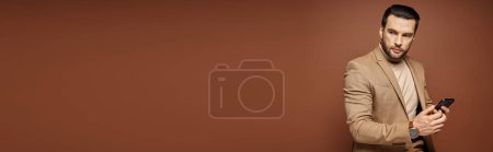 Téléchargez les photos : Bel homme d'affaires en tenue élégante vérifiant son smartphone sur fond beige, bannière - en image libre de droit