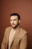 portrait of attractive man in elegant attire looking at camera on beige backdrop, handsome executive magic mug #692773964