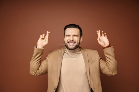 Téléchargez les photos : Portrait d'homme séduisant en tenue élégante souriant avec les doigts croisés sur fond beige - en image libre de droit
