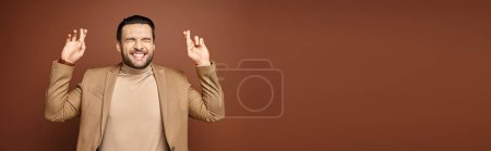 Téléchargez les photos : Bannière de l'homme attrayant en tenue élégante souriant avec les doigts croisés sur fond beige - en image libre de droit