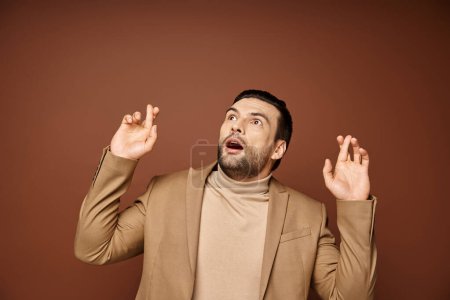 astonished man in elegant attire with his fingers crossed looking up on beige background
