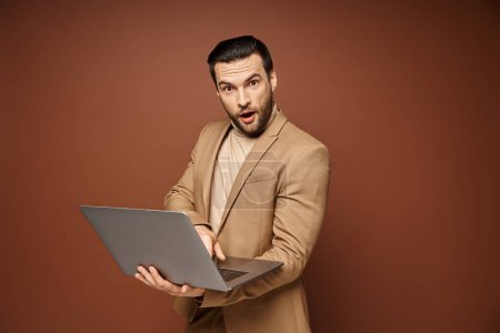 Photo for Shocked and handsome professional using his laptop while working remotely on beige background - Royalty Free Image