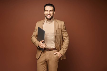 Téléchargez les photos : Homme d'affaires heureux en tenue élégante debout avec son ordinateur portable sur fond beige, travail à distance - en image libre de droit