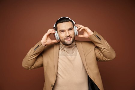 Charismatischer Mann in eleganter Kleidung genießt Musik in seinen drahtlosen Kopfhörern auf beigem Hintergrund