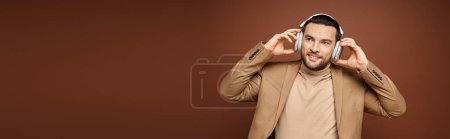 Téléchargez les photos : Homme charismatique en tenue élégante profitant de la musique dans ses écouteurs sans fil sur beige, bannière - en image libre de droit