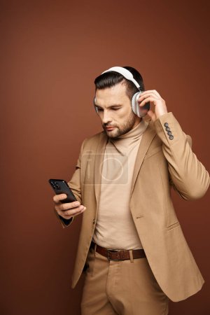 Téléchargez les photos : Bel homme dans les écouteurs sans fil en utilisant son smartphone sur fond beige, âge numérique - en image libre de droit
