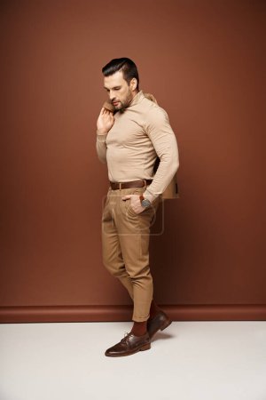 Photo for Stylish man in turtleneck holding his jacket over shoulder and posing with hand in pocket on beige - Royalty Free Image