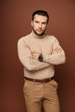 Determined and handsome man in turtleneck posing with crossed arms and sharp gaze