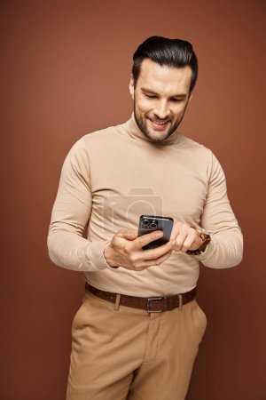 glücklicher Mann mit Borsten im Rollkragen mit seinem Smartphone auf beigem Hintergrund, Social Media