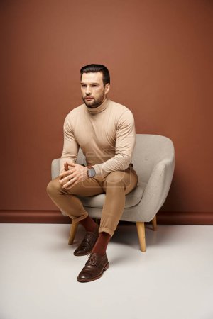 schöner und selbstbewusster Mann mit Borsten sitzt auf einem bequemen Sessel auf beigem Hintergrund