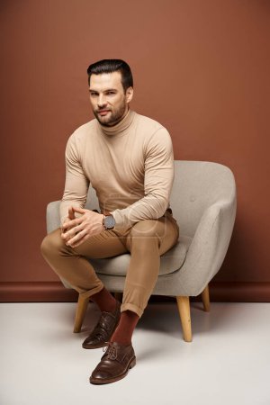 handsome and sly man with bristle sitting on comfortable armchair on beige background