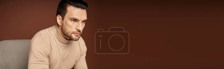 Photo for Portrait of handsome and serious man in turtleneck sitting on armchair on beige background, banner - Royalty Free Image