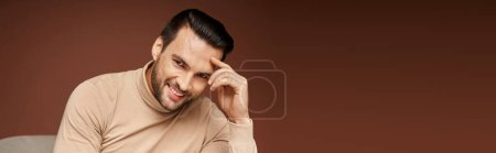 portrait of handsome man in turtleneck looking at camera and smiling on beige background, banner