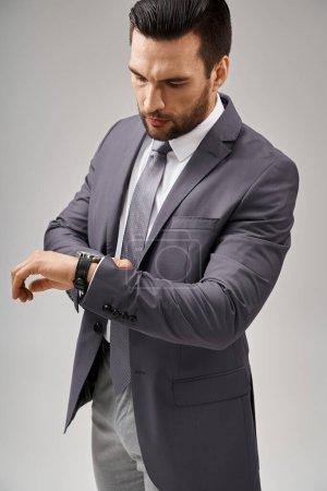 bel homme d'affaires posant dans un costume élégant vérifiant sa montre sur fond gris, élégance