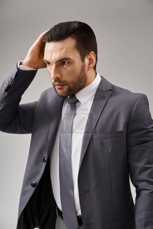 hombre guapo en ropa formal con corbata ajustando su cabello sobre fondo gris, moda corporativa