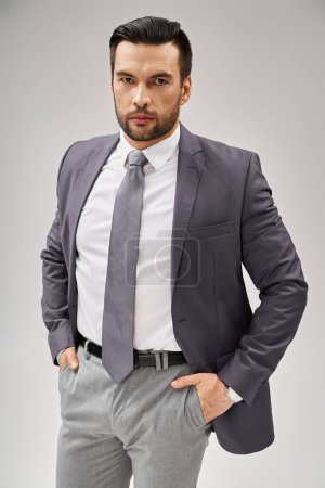 Charismatischer Geschäftsmann im Anzug posiert mit selbstbewusster Haltung und blickt vor grauem Hintergrund in die Kamera