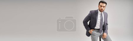 Téléchargez les photos : Bel homme d'affaires en tenue formelle posant la main dans la poche et assis sur un tabouret haut, bannière - en image libre de droit