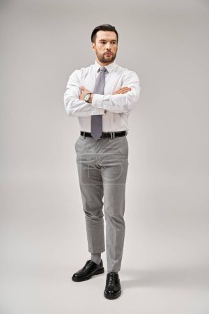 Téléchargez les photos : Pleine longueur de l'homme d'affaires en costume debout avec les bras croisés tout en posant sur fond gris - en image libre de droit