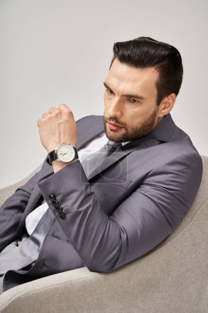 Foto de Retrato de empresario pensativo en traje elegante sentado en sillón cómodo sobre fondo gris, 30s - Imagen libre de derechos