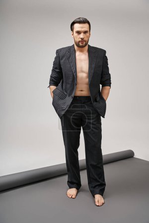 Kühnes Mode-Statement, gutaussehender und hemdsloser Mann im Nadelstreifenanzug posiert auf grauem Hintergrund
