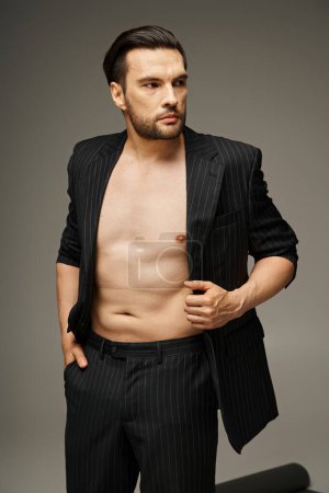 Mode-Statement-Konzept, wagemutiger und hemdloser Mann im Nadelstreifenanzug posiert auf grauem Hintergrund