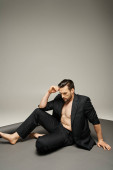 stylish and handsome man with bare chest posing in pinstripe suit on grey background, fashion t-shirt #692776476